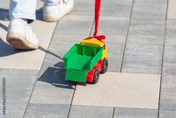 Fototapeta The child rolls a toy car on a rope behind him.