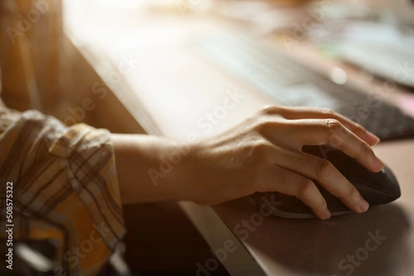 Fototapeta Close-up image, Female hand using a wireless computer mouse at her office desk.