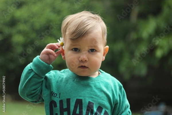 Fototapeta closeup face of funny teenage boy with freckles and camomile behind his ear on sunny grass background