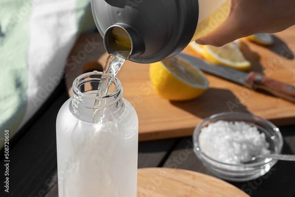 Fototapeta Cooking fresh homemade isotonic from natural ingredients - salt, lemon and mineral water. Pouring into a bottle