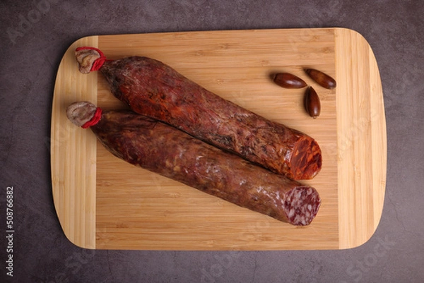 Fototapeta Iberian sausage and Iberian chorizo on cutting board and dark gray table.