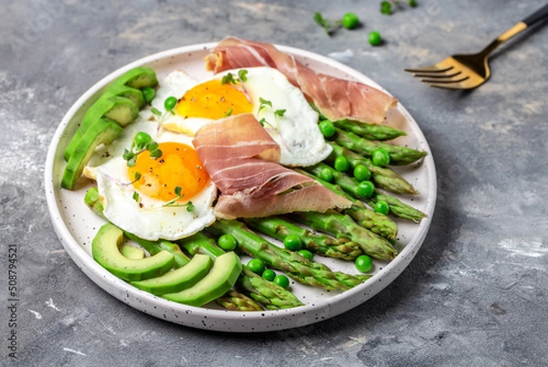 Obraz Tasty breakfast. avocado, asparagus, jamon, ham, prosciutto and fried egg on white plate. banner, menu recipe place for text, top view