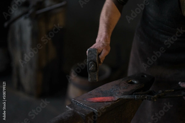 Fototapeta blacksmith hitting a red-hot iron with a hammer