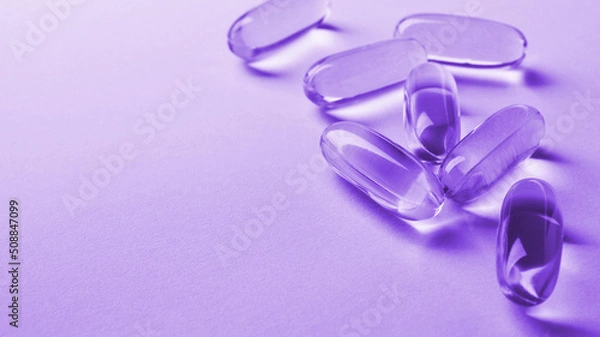 Fototapeta Fish oil softgels lie on a light surface. Vitamin and a healthy lifestyle. Purple tinted background or backdrop. Copyspace on the left. Softgel close up. Omega-3 fatty acid capsule. Macro