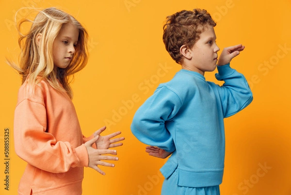 Fototapeta happy little children of school age stand in bright clothes on a yellow background and dance vigorously