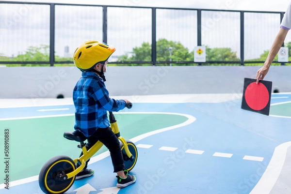 Fototapeta Asian cute child learns to ride a balance bike with a yellow helmet. Stop waiting for the red light , learning traffic rules.