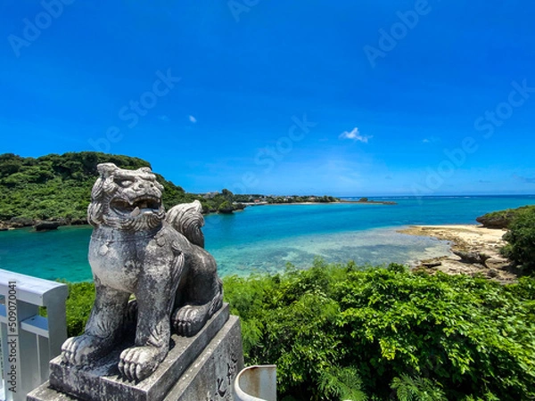 Obraz 晴れた暑い夏の沖縄県うるま市にある宮城島と伊計島をつなぐ赤い伊計大橋の前にあるシーサー