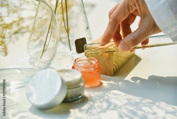 Fototapeta Scientist mixing natural skin care beauty products, Organic botany extraction and scientific laboratory glassware, Blank label cosmetic container for branding mock-up.