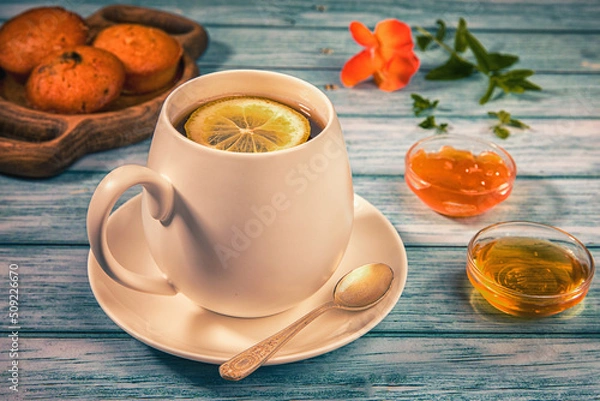 Obraz Breakfast - cake and cup of tea on wooden table decorated with flowers and jam.Close up.