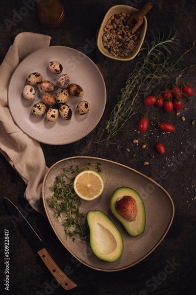 Obraz Ripe avacado decoreted on the plate and raw Quail eggs on the dark table.Healthy breakfast, vegetable food.