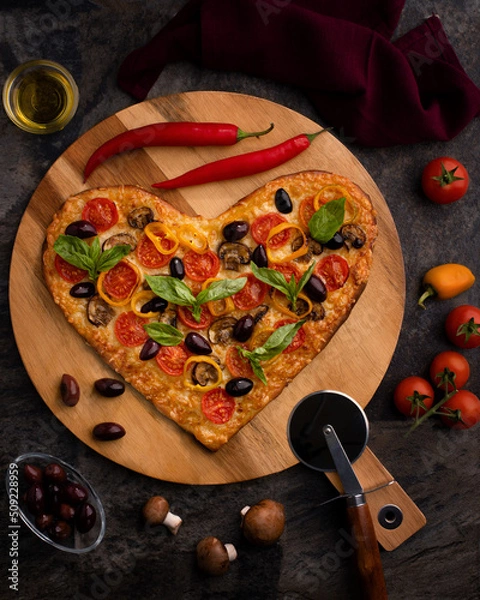 Obraz Wooden board with homemade  heart-shaped pizza with ingredients on black background. Valentine's Day celebration.