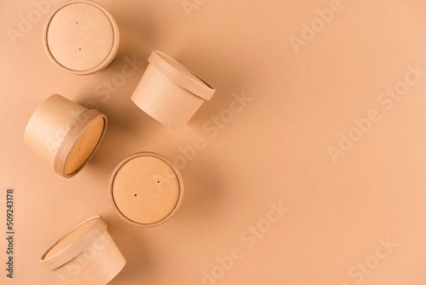Fototapeta Brown disposable kraft paper soup or ice cream container, cup with paper cap over light brown background with copy space, mockup. Sustainable food packaging concept