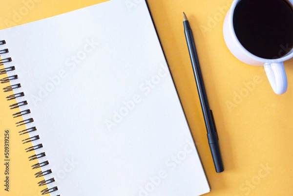 Fototapeta Directly above view of notepad, pen and coffee cup on yellow background.