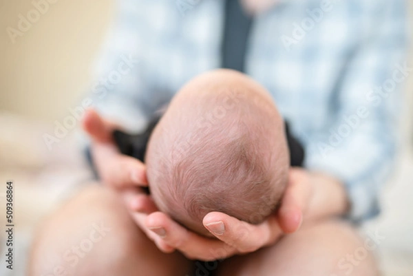 Fototapeta The father holds the newborn on his lap with his head to the camera. Focus on the child's head. The concept of child care and protection