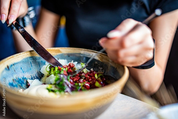 Fototapeta Young woman hand eating beef tartare using knife and fork fom bowl in cafe