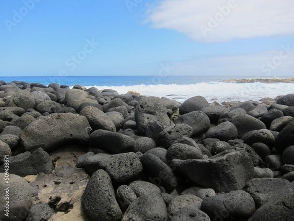 Obraz Black volcanic rocks against a deep blue sea. Waves, blue sky and white clouds. Rocky beach at Lehia Park, Hilo, Big Island of Hawaii.