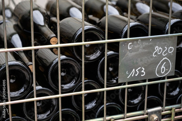 Obraz Full bottles of wine lying in a container, freshly corked. In the foreground, the fence of the container.