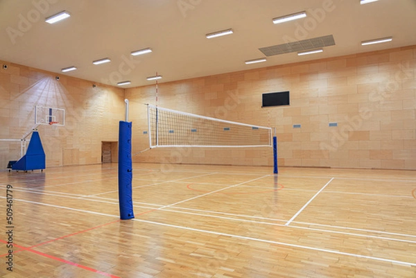 Fototapeta Volleyball net in an empty gym with a mobile basketball hoop in the background