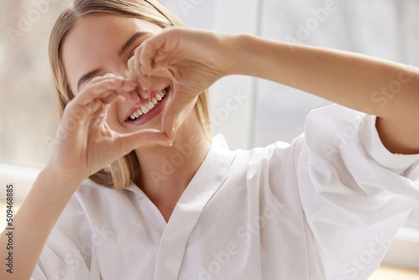 Fototapeta Healthy Tooth. Smiling Woman Showing Heart Sign wit Hands. Beautiful Happy Girl Model with Healthy White Smile and Natural Makeup. Stomatology and Teeth Care concept