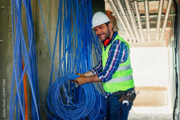 Fototapeta A skilled electrician in construction checking cables for building electric network.