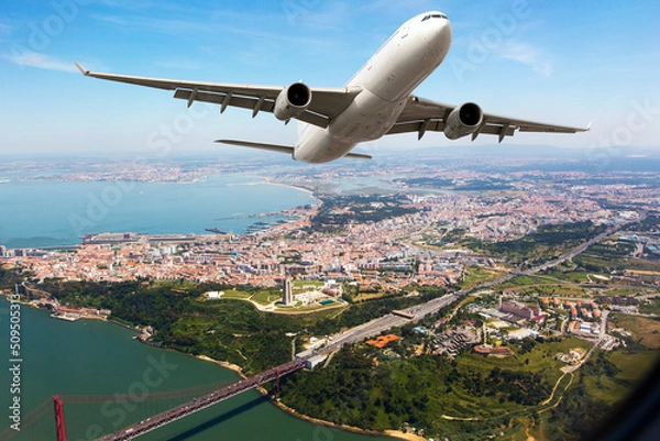 Fototapeta White passenger plane in flight. The plane flies against a background of city and river.