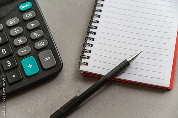 Fototapeta Calculator, pen, notepad lie on a gray surface. Open spring-loaded notebook with blank sheets. Close-up.