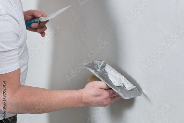 Obraz the master holds a spatula with a mortar in his hand, applying decorative plaster to the wall