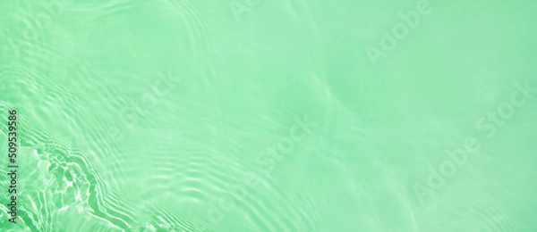 Fototapeta Abstract summer banner background Transparent green clear water surface texture with ripples and splashes. Water wave in sunlight, copy space, top view Cosmetics moisturizer micellar toner emulsion