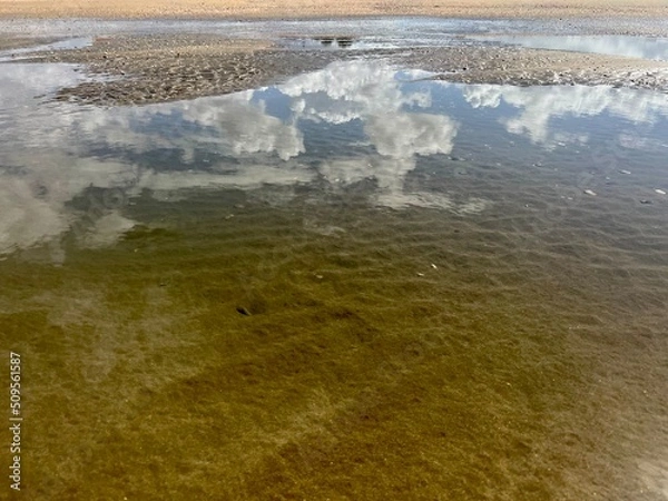 Obraz puddle on beach shore with reflected clouds