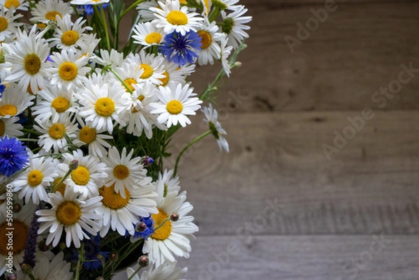 Fototapeta Midsummer bouquet of summer flowers white daisies and blue cornflowers in the vase on wooden background with copy space. Top view