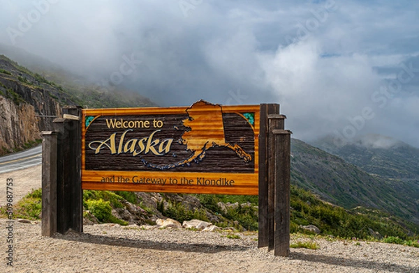 Fototapeta Skagway, Alaska, USA - July 20, 2011: Klondike highway to Canada. Colorful Welcome sign near the border. Cloudscape in back.