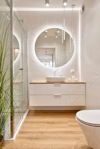 Fototapeta Luxury bathroom with glass to shower, round mirror with led lights, stylish washbasin and wooden floor. Modern interior of bathroom with wc and bath. Vertical.