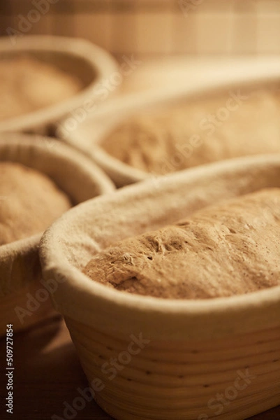 Fototapeta Process of making wheat bread at home. Proofing of the dough in rattan baskets. The concept of healthy homemade food. Vertical photo.