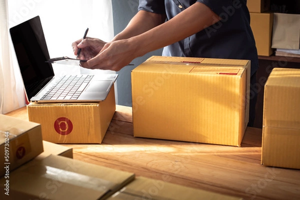 Fototapeta Young entrepreneur business owner work at home, small business startup receive order client and take note working with report and pack the product on purchase delivery online to sending destination.
