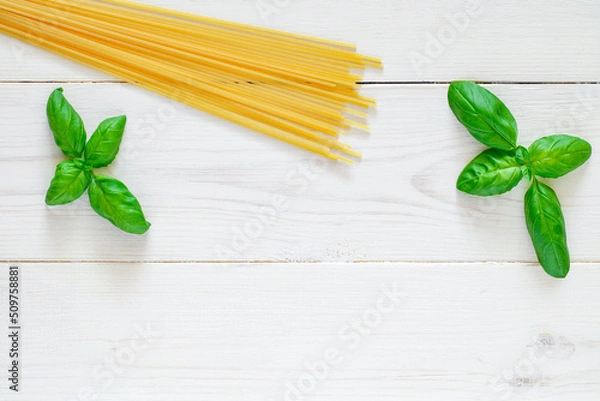 Fototapeta Spaghetti, raw pasta, basil leaves on white wooden board background, top view, space to copy text.