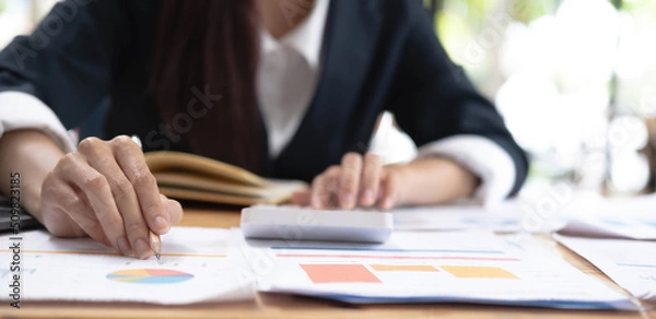 Fototapeta Close up of Hand business woman holding pen pointing on chart summary report and calculate finance.