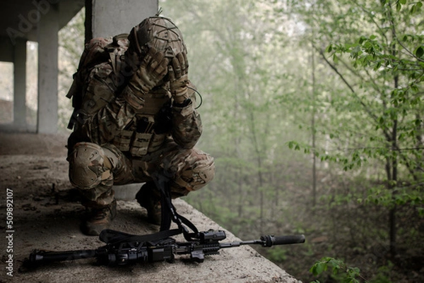 Fototapeta Military soldier in uniform sitting on his knees, releasing his head in front of the machine gun. Loss of a combat partner. Defeat in battle