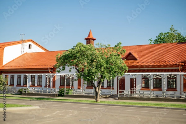 Fototapeta One-storey building with red-tiled roof and green tree in front of entrance
