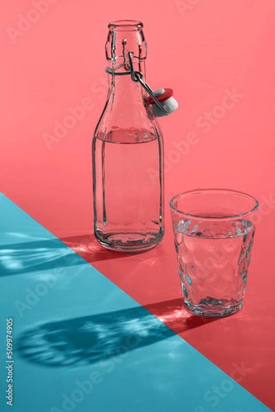 Obraz Vintage bottles and glass with sun light shadows or reflection on pink-blue background.