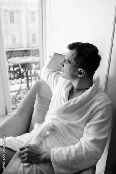 Fototapeta in the photo, a smug man in a bathrobe in hotels lying down enjoying the view from the window