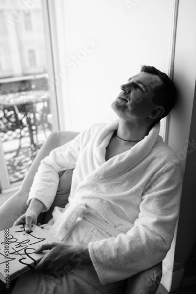 Fototapeta in the photo, a smug man in a bathrobe in hotels lying down enjoying the view from the window