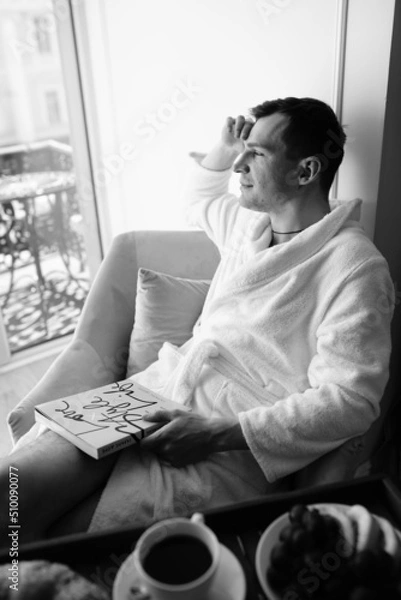 Fototapeta in the photo, a smug man in a bathrobe in hotels lying down enjoying the view from the window