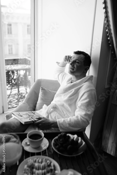 Fototapeta in the photo, a smug man in a bathrobe in hotels lying down enjoying the view from the window