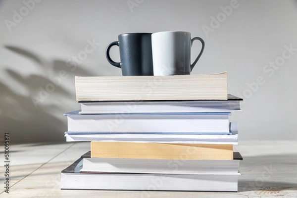 Fototapeta White and gray coffee cups on a stack of books. Home office concept, back to school
