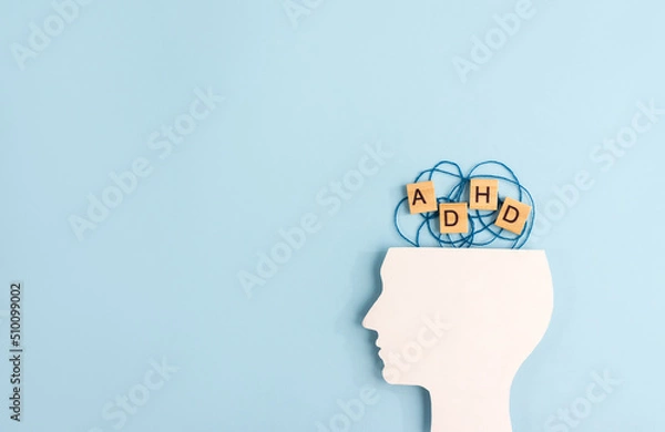 Fototapeta Silhouette of human head and wooden blocks with the letters ADHD on pastel background. Creative concept of attention deficit hyperactivity syndrome. Copy space