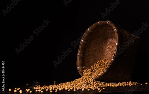 Fototapeta Photo of soybean seeds spilling from their container on a black background. Suitable for design elements of agricultural products, healthy food, and organic food.