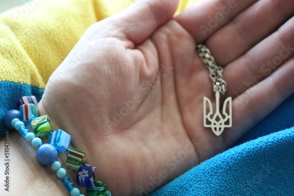 Fototapeta Ukrainian woman  holds a pendant in the form of the coat of arms of Ukraine in her hand