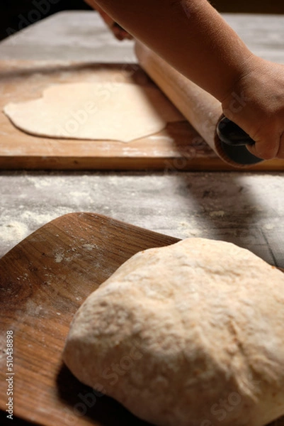Obraz close-up blurred shot of child's hands kneading fajita bread with rolling pin, ball of bread dough on wooden plate