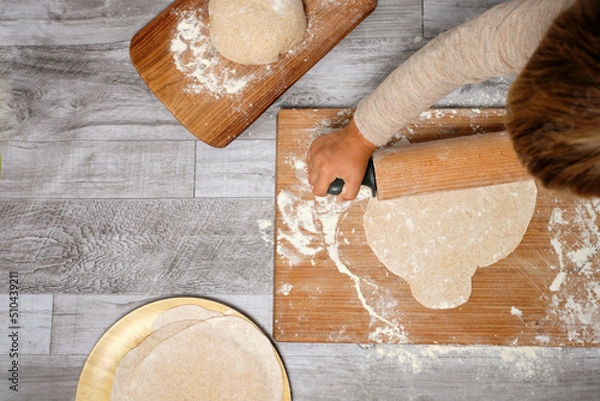 Fototapeta Top view of boy kneading pizza with wooden rolling pin surrounded by flour. copy space