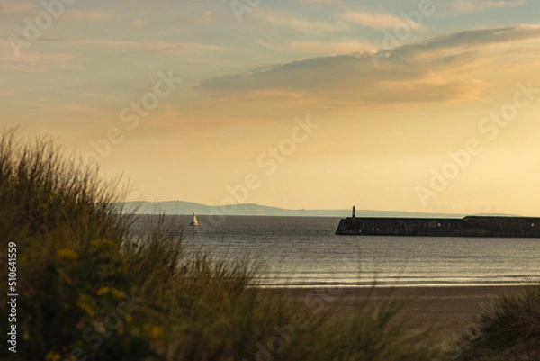 Fototapeta Sunset on the beach with breakwaters and a lighthouse